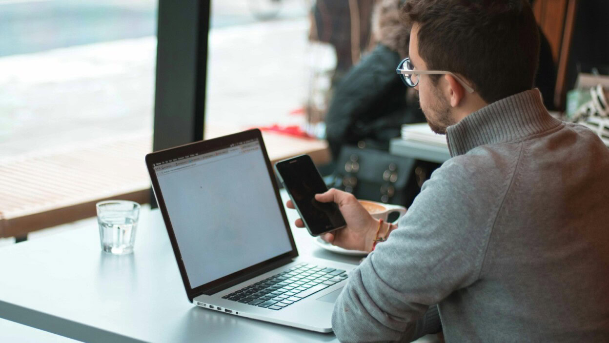 man sitting near table with laptop and smartphone near window